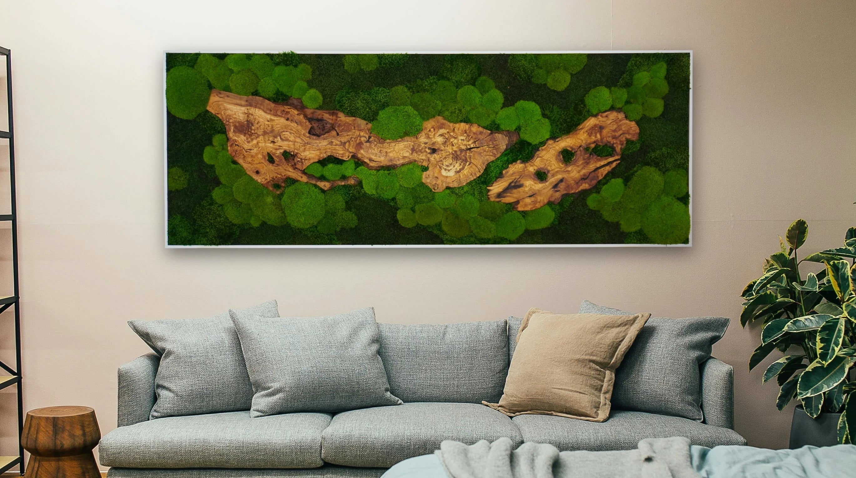 Handgemachtes Moosbild als Sonderanfertigung mit grünen Moosen und edlem Olivenholz in einem silberfarbenen Rahmen über einer Couch.