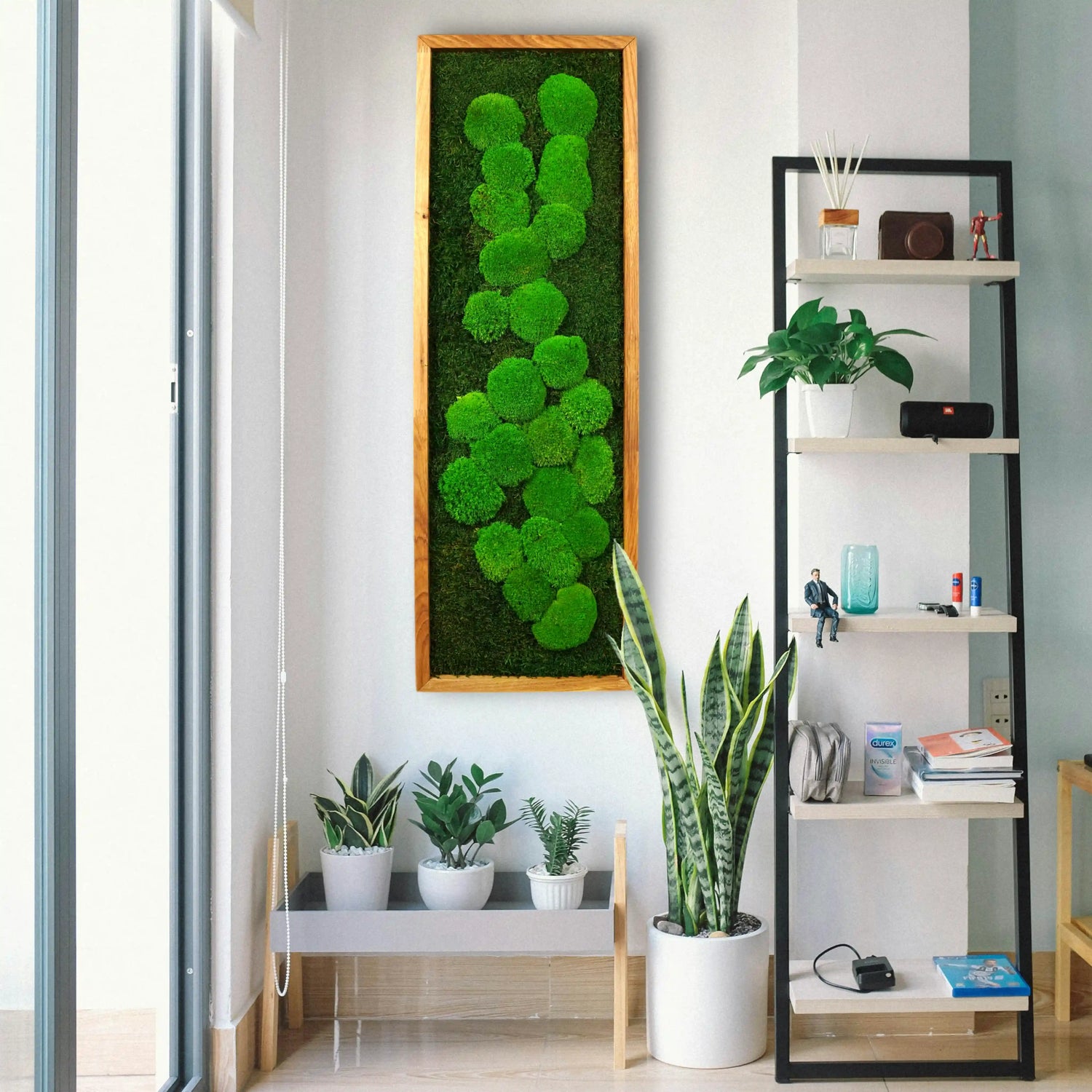 Handgemachtes einfaches Moosbild „Abstract“ in einem Holzrahmen - kunstvolle Wanddekoration aus grünen Moosen an einer weißen Wand umgeben von Pflanzen - Frontansicht.