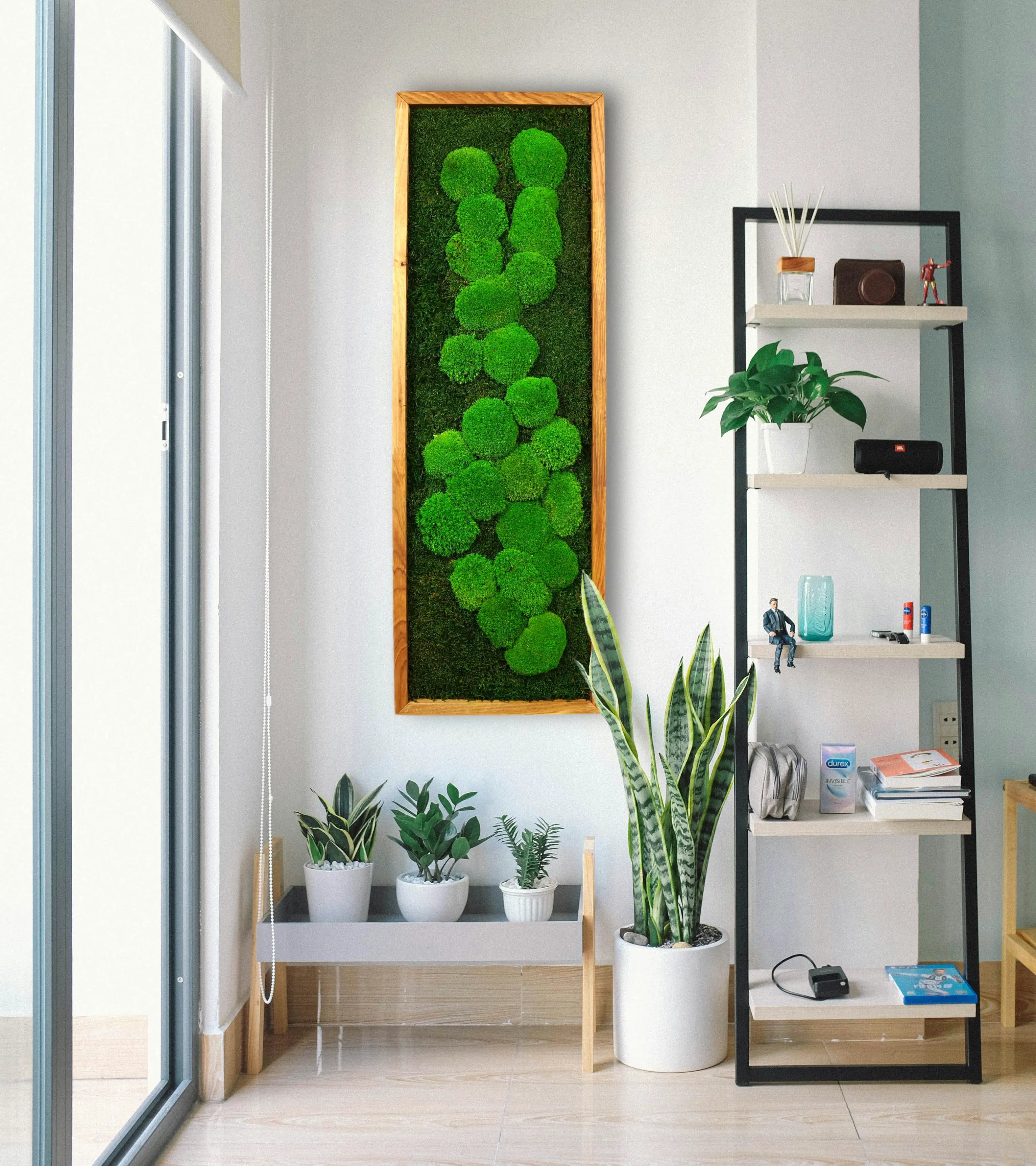 Handgemachtes einfaches Moosbild „Abstract“ in einem Holzrahmen - kunstvolle Wanddekoration aus grünen Moosen an einer weißen Wand umgeben von Pflanzen - Frontansicht.