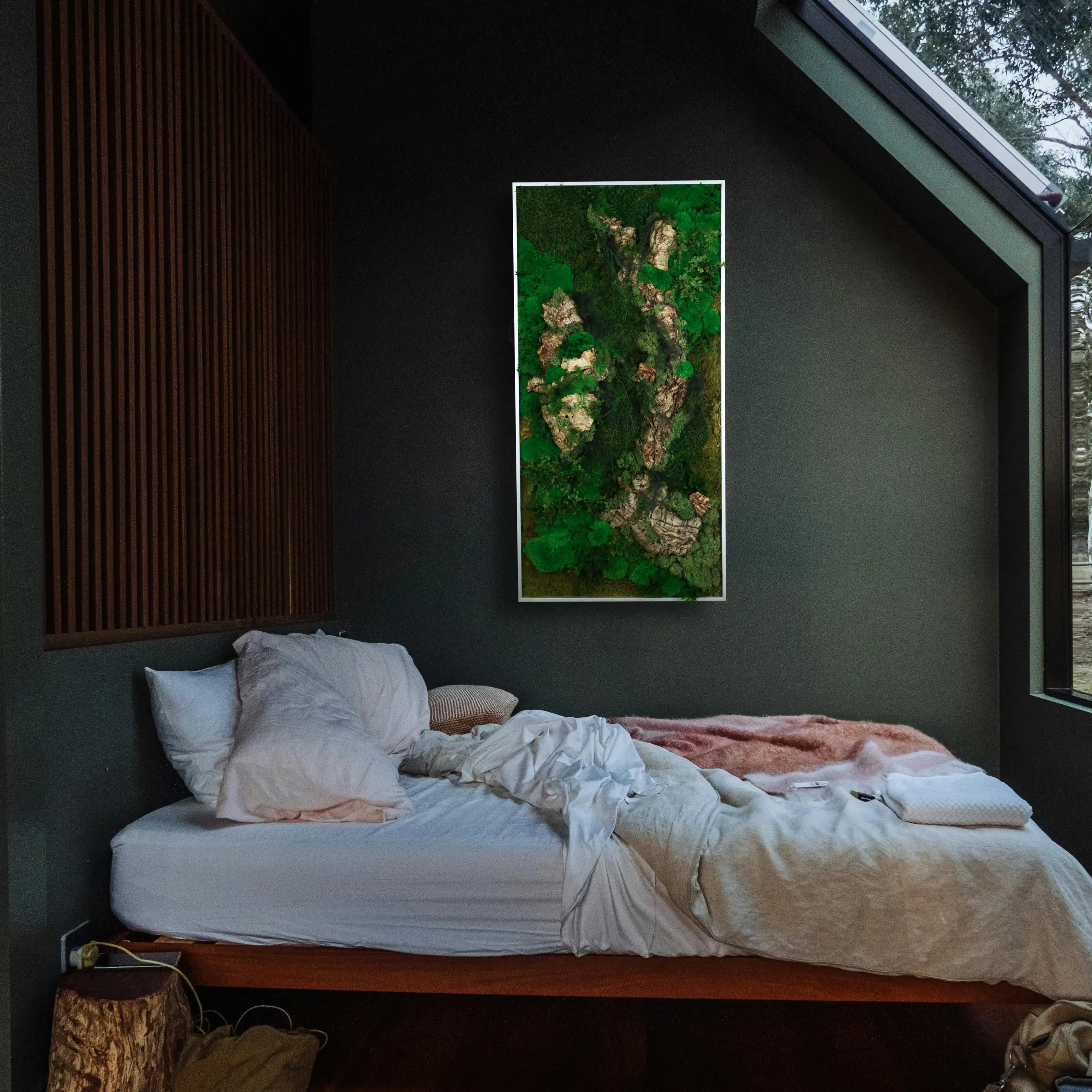 Aufwendig gestaltetes Moosbild mit dem Namen „Canyon“ in einem silberfarbenen Rahmen - eine kunstvolle Wanddekoration aus grünen Moosen, Pflanzen und Kork in einem modernen Schlafzimmer.