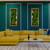 Detailreich dekoriertes Moosbild „Landscape“ in einem Holzrahmen - eine farbenfrohe Wanddekoration aus Moosen und verschiedenen Pflanzen über einer gelben Couch.